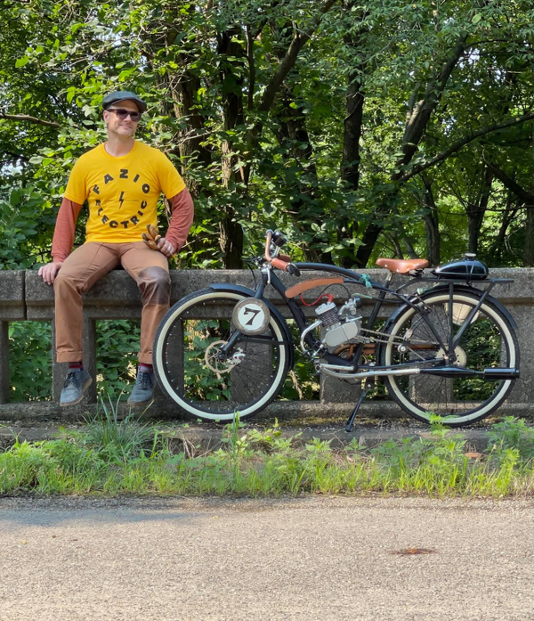 a man sitting with his parked motorized bike on the sidewalk