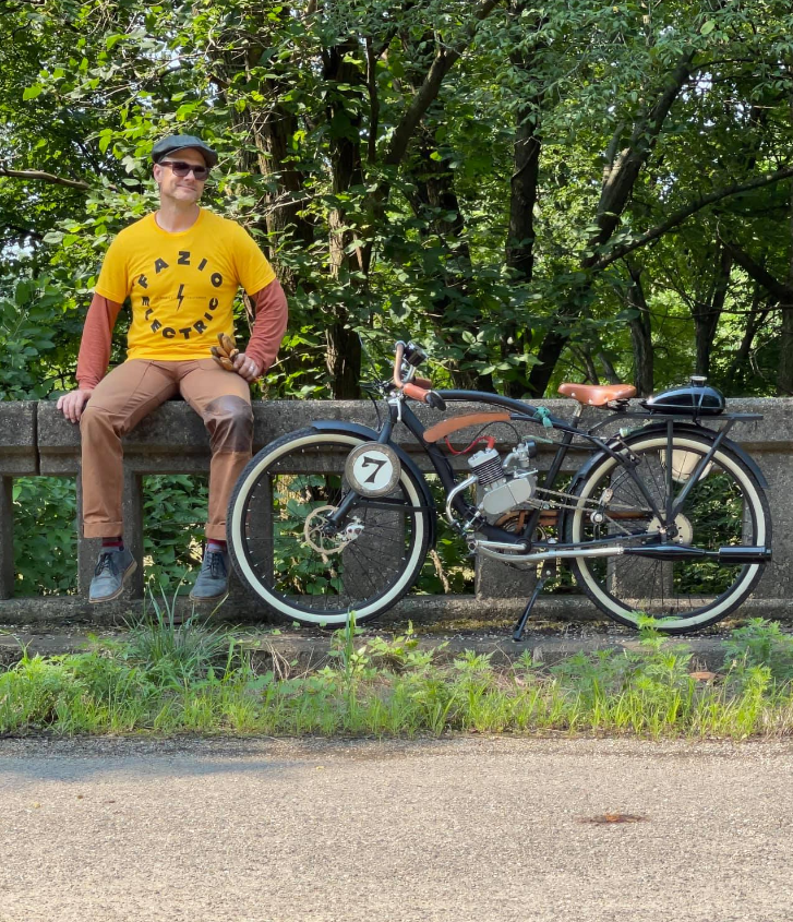 a man sitting with his parked motorized bike on the sidewalk